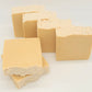 Four "I LOVE This Bar" goat milk soaps by Amillia Acres, in a luxurious beige with textured tops, are artistically arranged on a white background. Two bars lie flat while two stand upright, highlighting their artisanal charm.