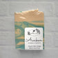 The "Awaken" goat milk soap by Amillia Acres features invigorating eucalyptus and spearmint scents, a teal and cream swirl design, and packaging with a goat silhouette wrapped in leafy branches.