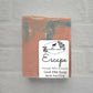 A 4 oz (113 g) bar of marbled pink and teal goat milk soap from Amillia Acres is wrapped in clear plastic. The label on the white background highlights "Escape Fragrance: Pineapple, Melon & Coconut," offering a rejuvenating experience.