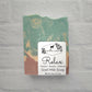 Displayed on a light textured surface, a bar of goat milk soap in green, cream, and brown tones is enriched with natural oils. The label reads: "Amillia Acres ~ Relax  | Goat Milk Soap - Coconut - Jasmine - Driftwood - Net wt. 4 oz (113 g)," beautifully showcasing handmade craftsmanship.