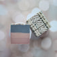 Amillia Acres' Sweater Weather Goat Milk Soaps: one with natural oils in gray, pink, and cream layers; the other with intricate swirls. A soft bokeh background accentuates these exquisite handmade soaps.