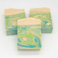 Three Awaken goat milk soap bars from Amillia Acres, featuring a marbled design in green, blue, and cream with eucalyptus and spearmint, are displayed against a plain white background.