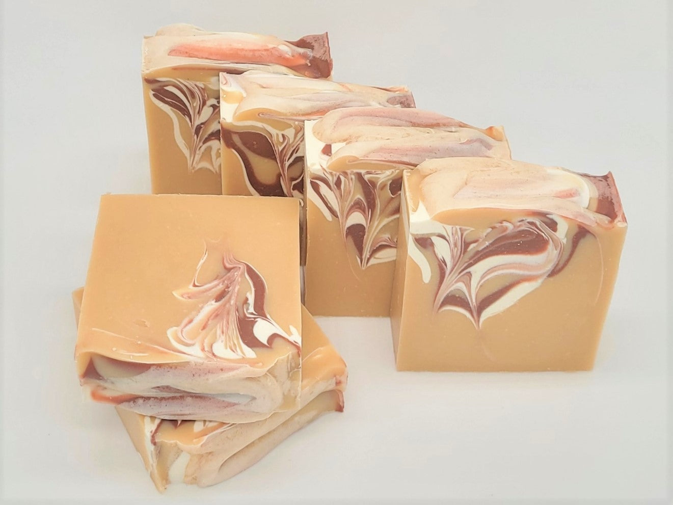 Five Comfort goat milk soap bars by Amillia Acres, featuring swirled shades of brown, cream, and pink, are arranged on a light surface. Infused with natural oils, the intricate marbled design on each bar adds an artistic touch.