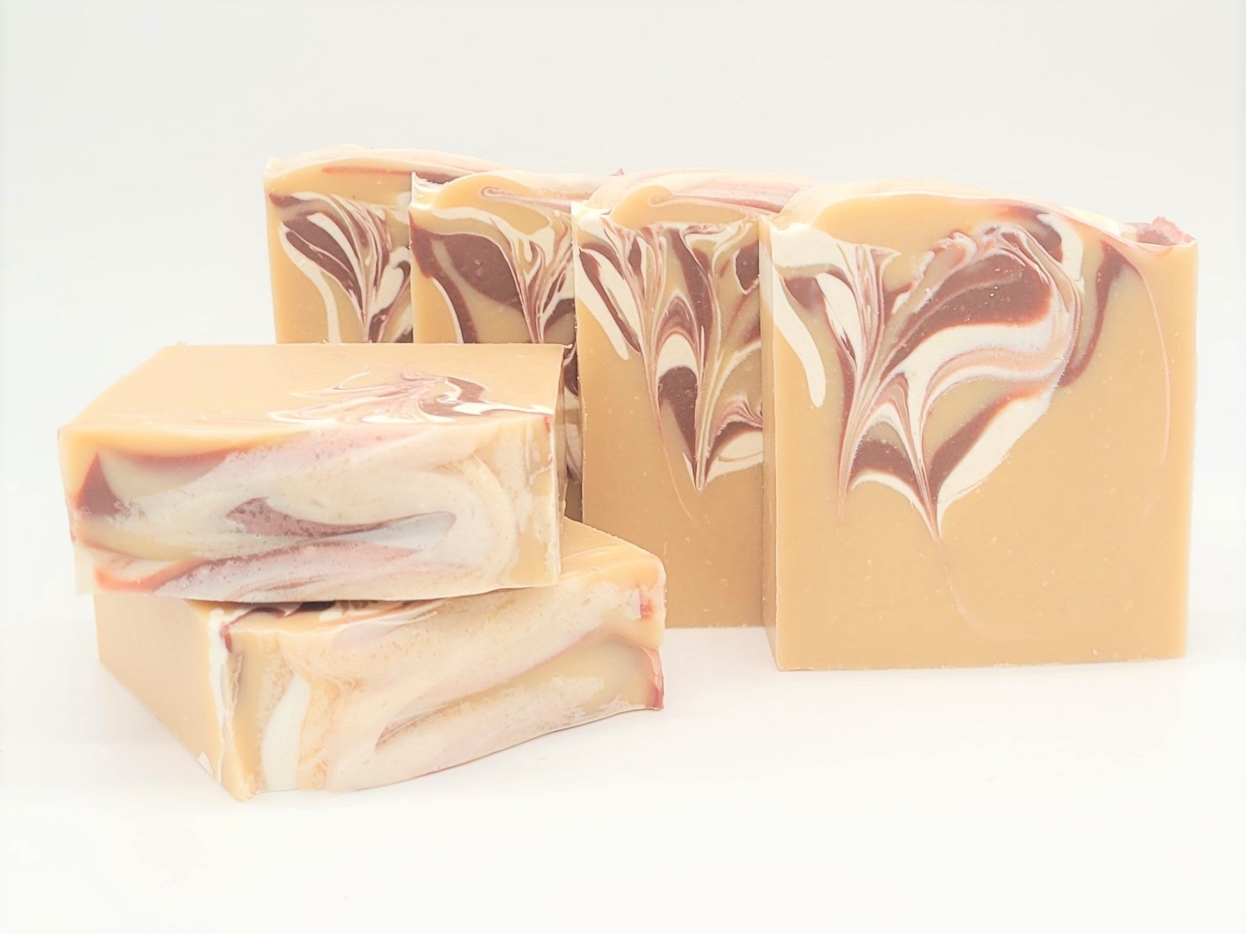 Five Comfort Goat Milk Soaps by Amillia Acres, crafted with natural oils and swirling cream, pink, and brown patterns, are displayed against a white background. Three bars stand upright while two lie flat in the foreground, showcasing their handmade beauty.